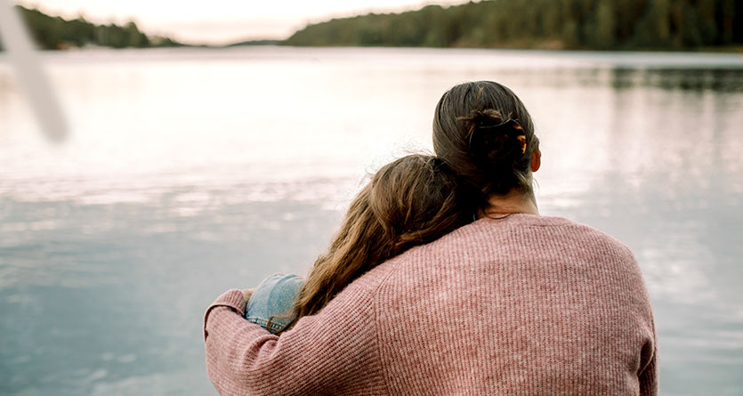 Mor och dotter kramas framför en sjö